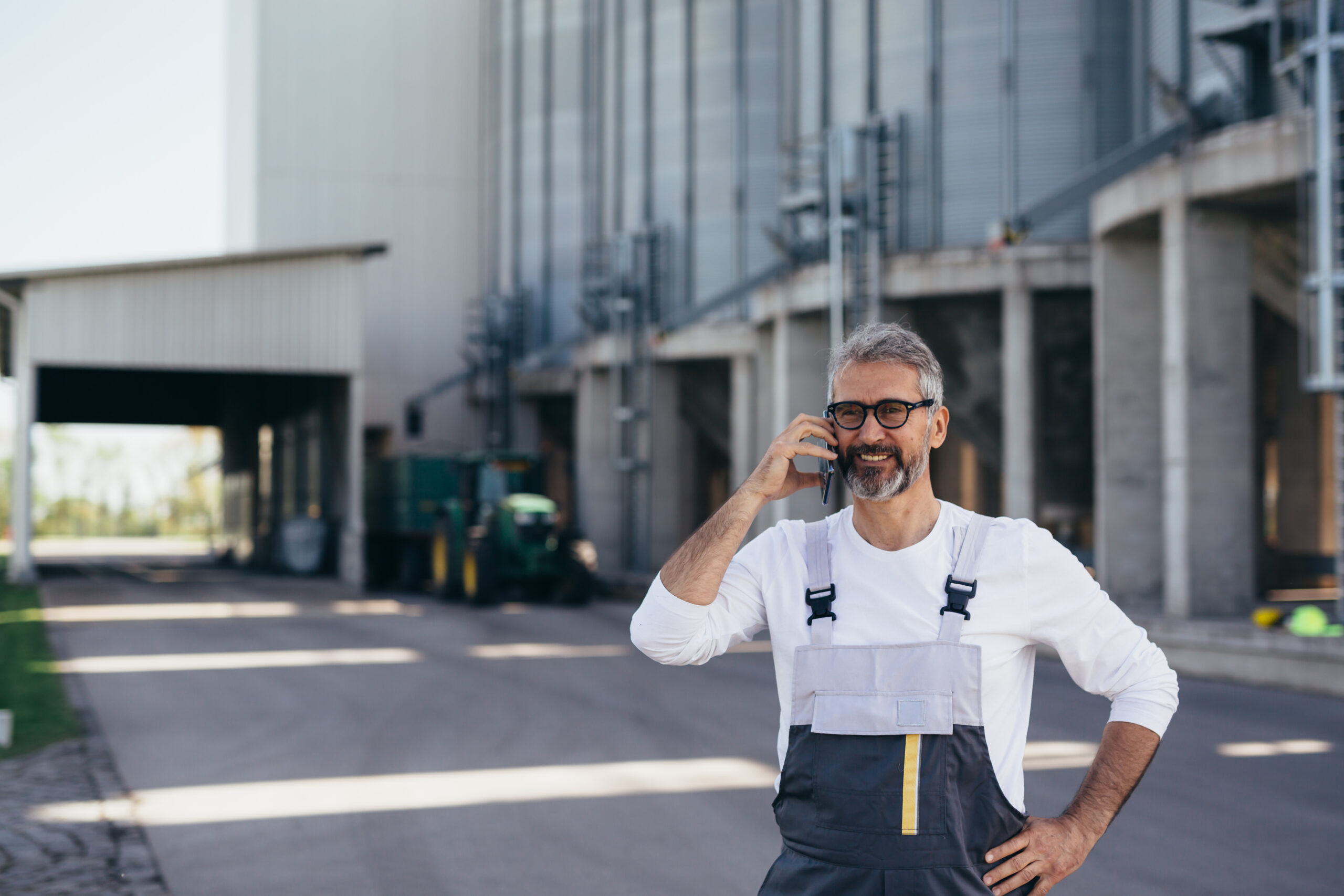 worker talking on mobile phone in front of grain silo outdoor