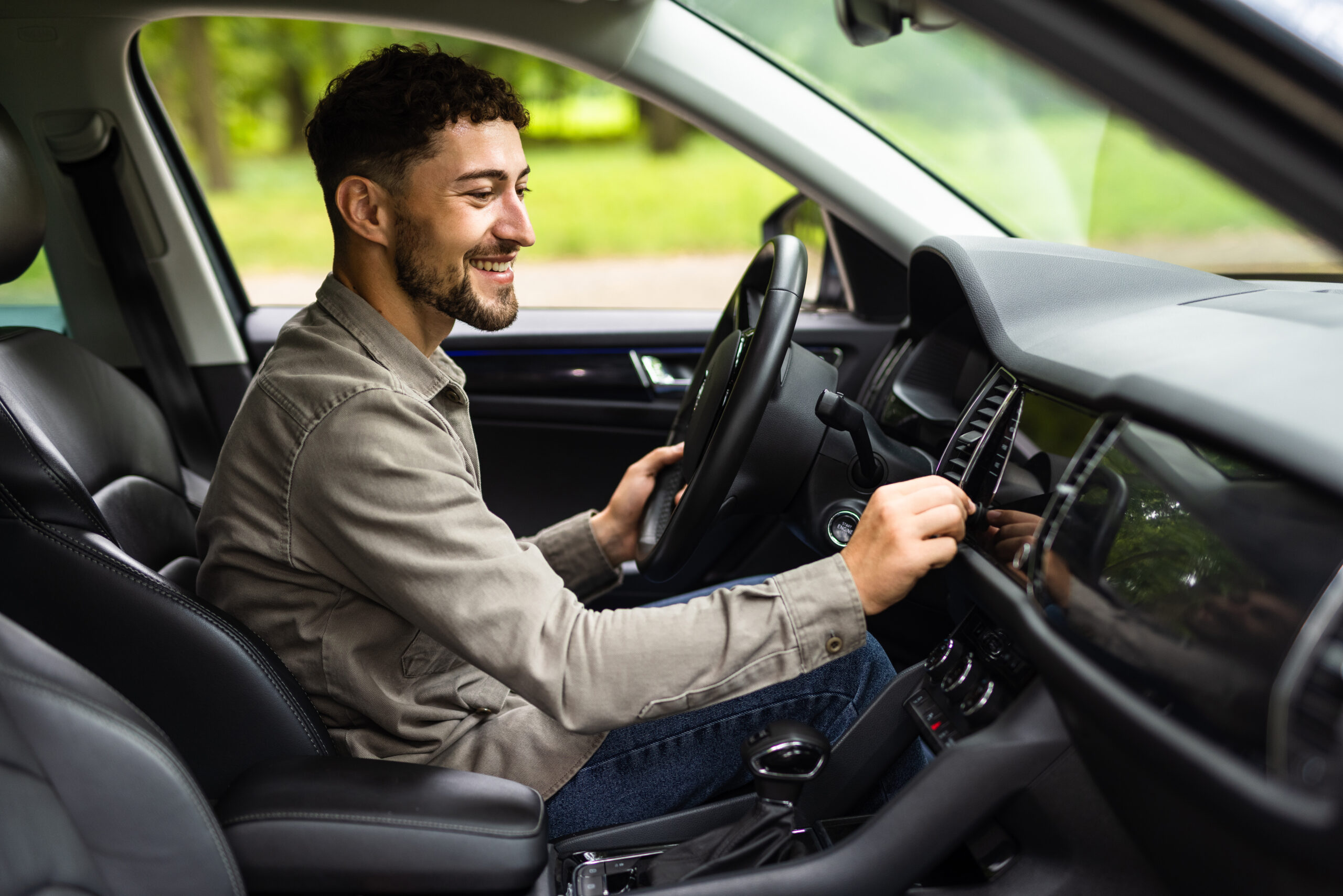 Young caucasian man sitting on car turning on radio at street