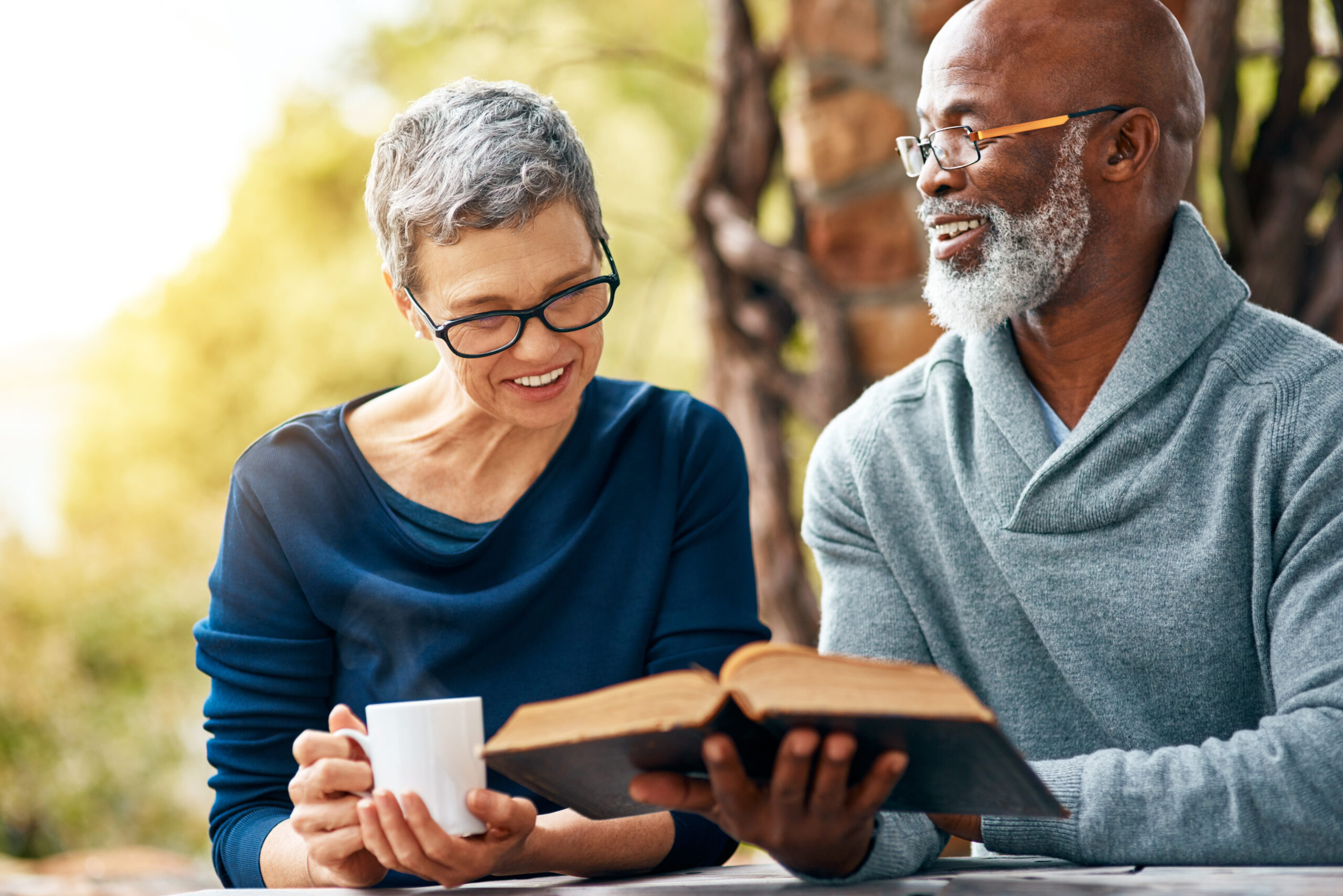 Senior, nature or happy couple with coffee or bible in spiritual religion for peace, guidance or learning. Book, interracial marriage and people in park for scripture, worship or prayer for faith.