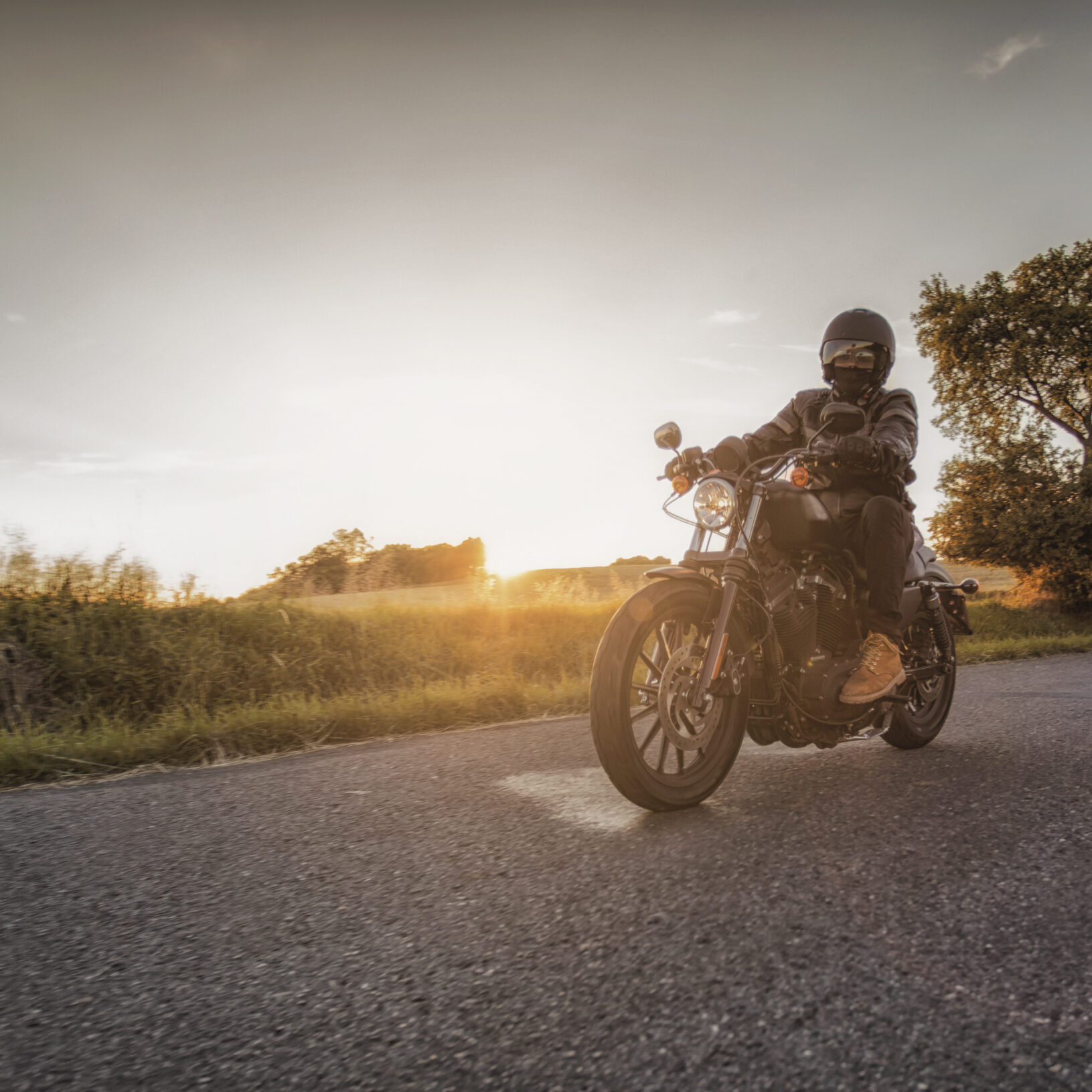 Biker rides his motorcycle along the road during beautiful sunset. Motorbiker's season starts now during spring time.
