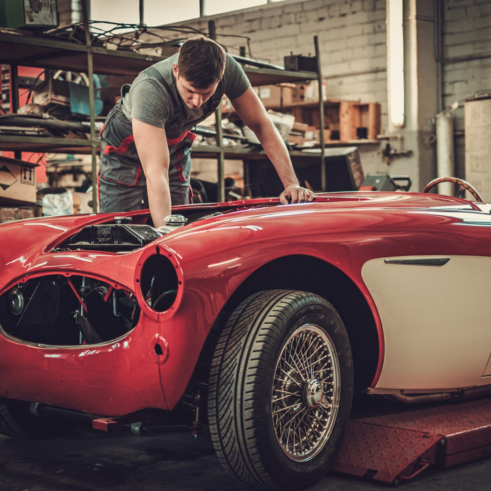 Mechanic working on classic car electrics in restoration workshop.