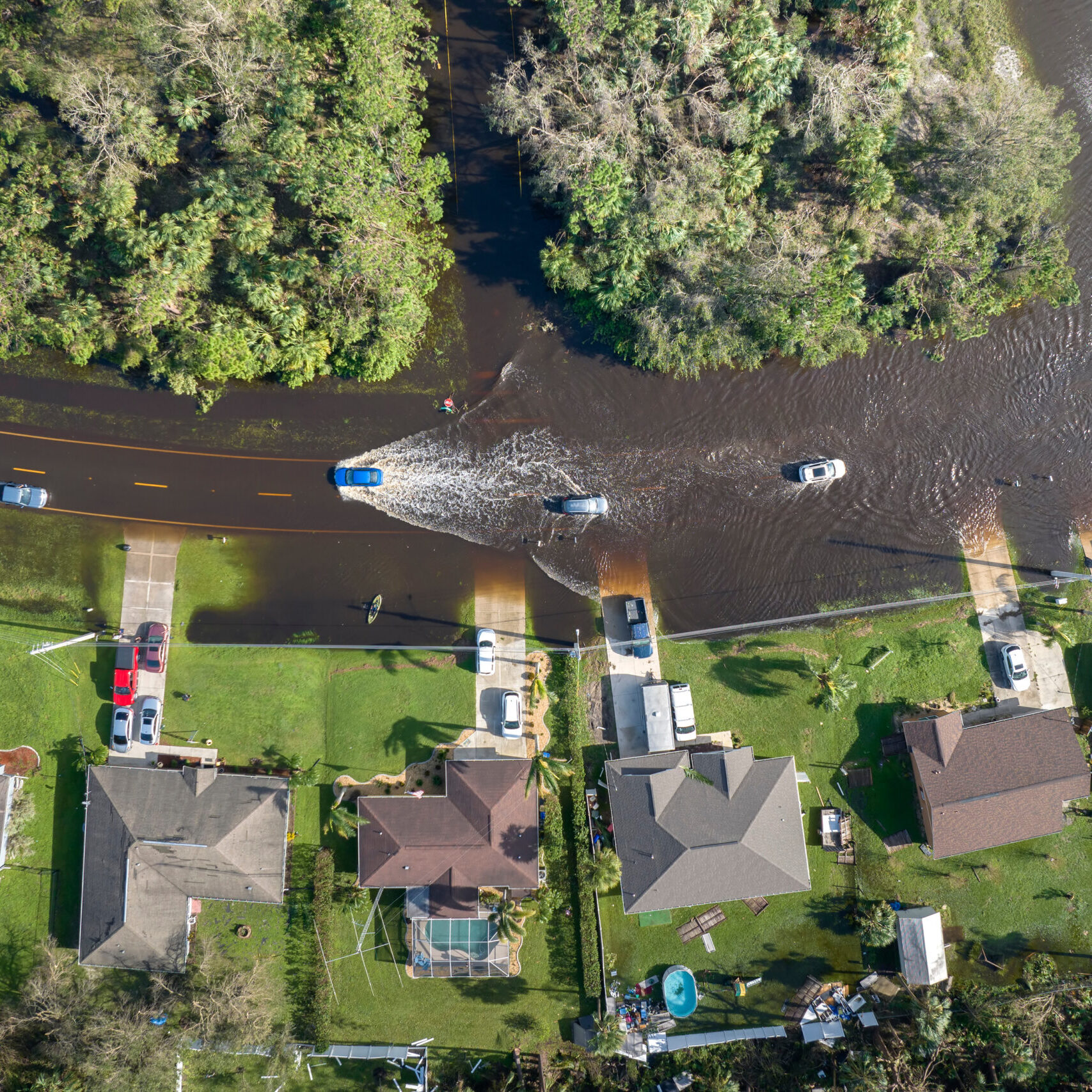 Hurricahe fainfall flooded Florida road with evacuating cars and surrounded with water houses in suburban residential area.