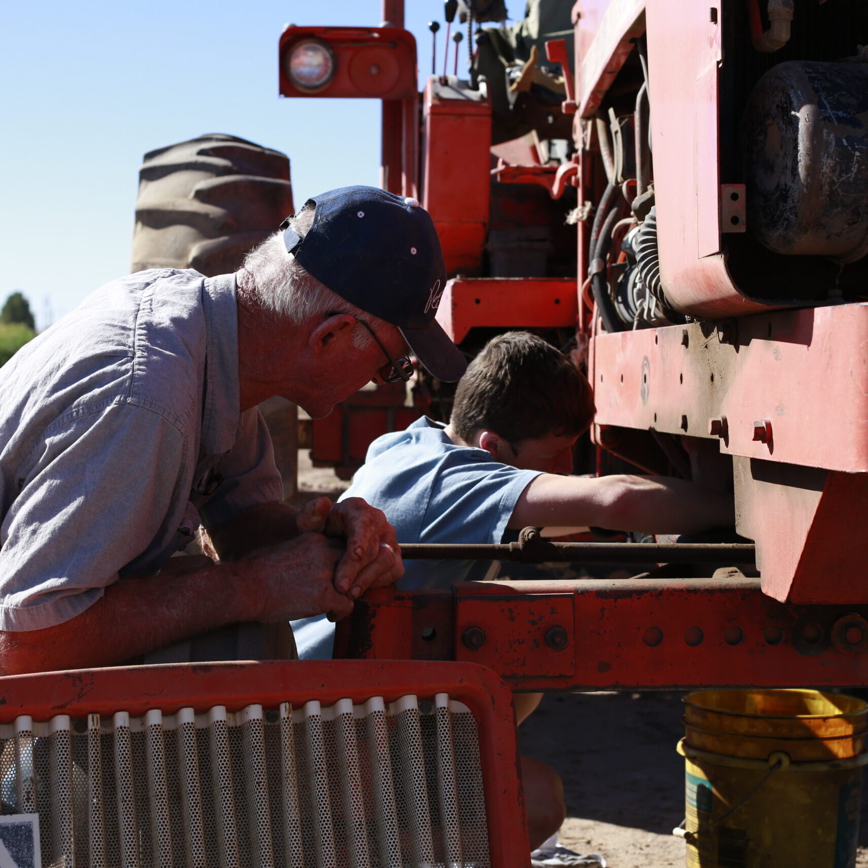 Grandfather is a farmer and teaching his grandson how to repair the tractor on his farm.