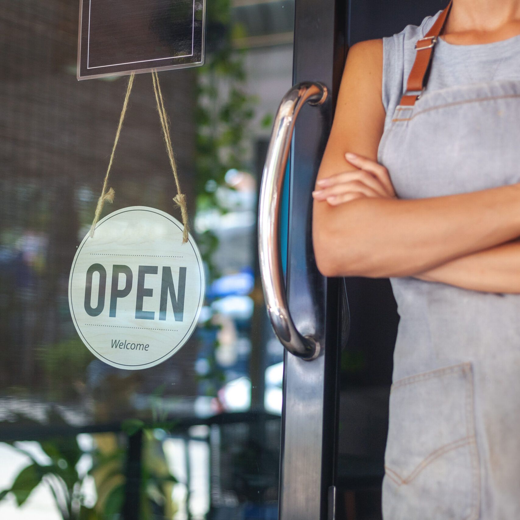 The woman is a waitress in an apron, the owner of the cafe stands at the door with a sign Open waiting for customers. Small business concept, cafes and restaurants