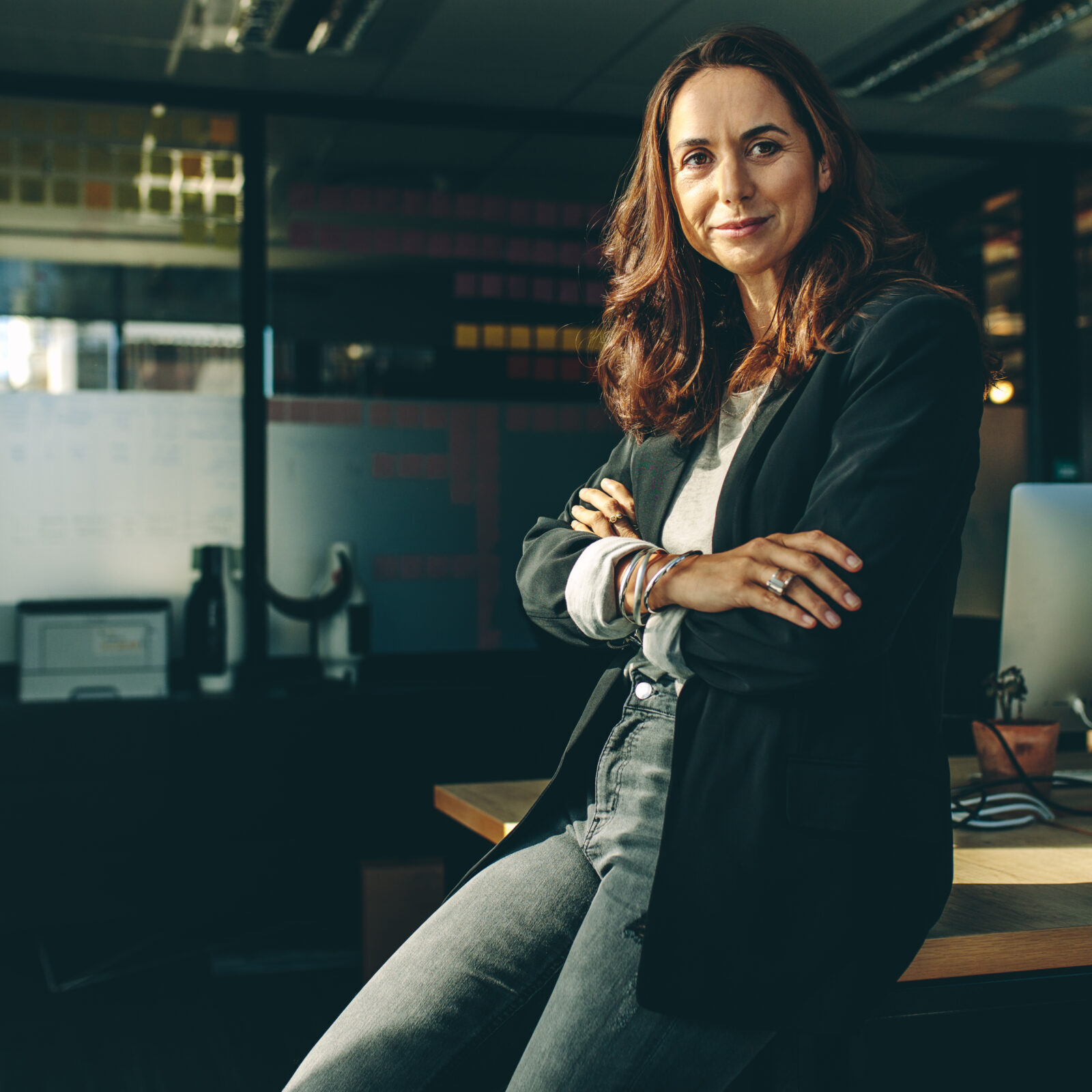 Mature businesswoman sitting on her desk. Confident female entrepreneur with her arms crossed looking at camera.