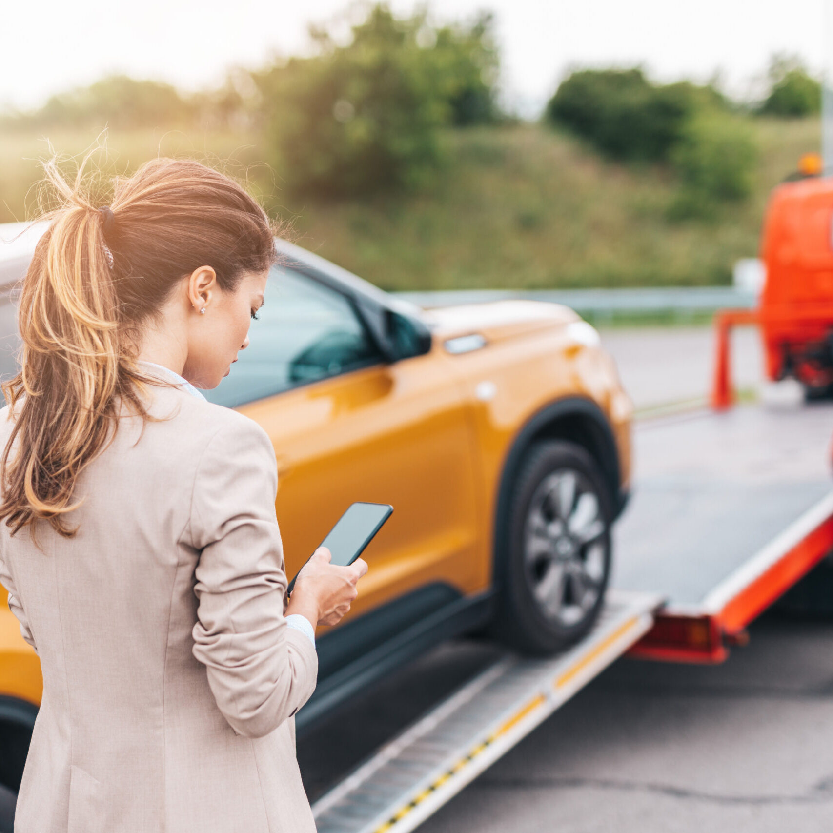 Elegant middle age business woman calling someone while towing service helping her on the road. Roadside assistance concept.