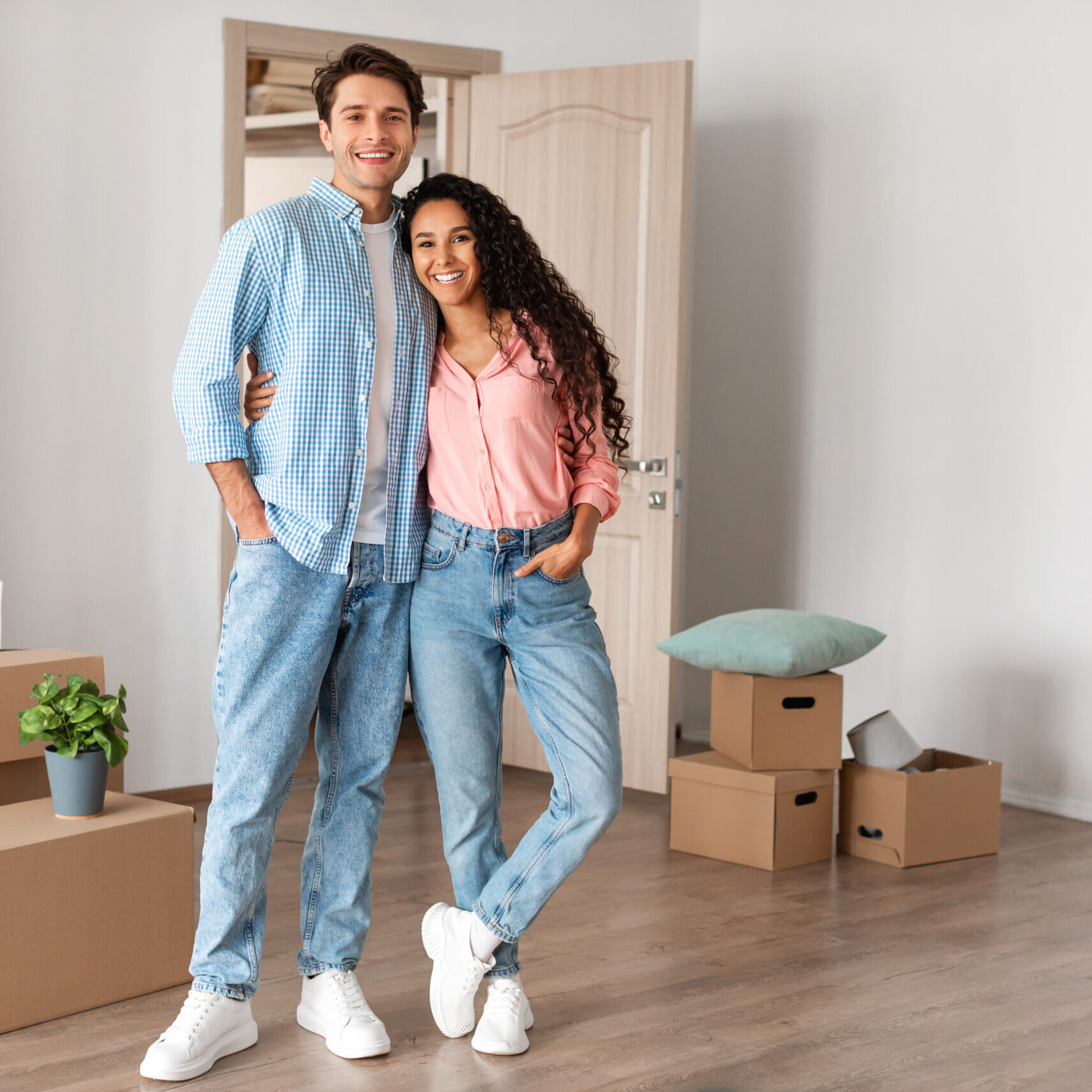 House Ownership. Happy Young Couple Standing In New Flat With Cardboard Boxes On Floor, Cheerful Guy And Lady Posing Hugging After Moving In Own Apartment. Insurance, Real Estate, Mortgage Concept