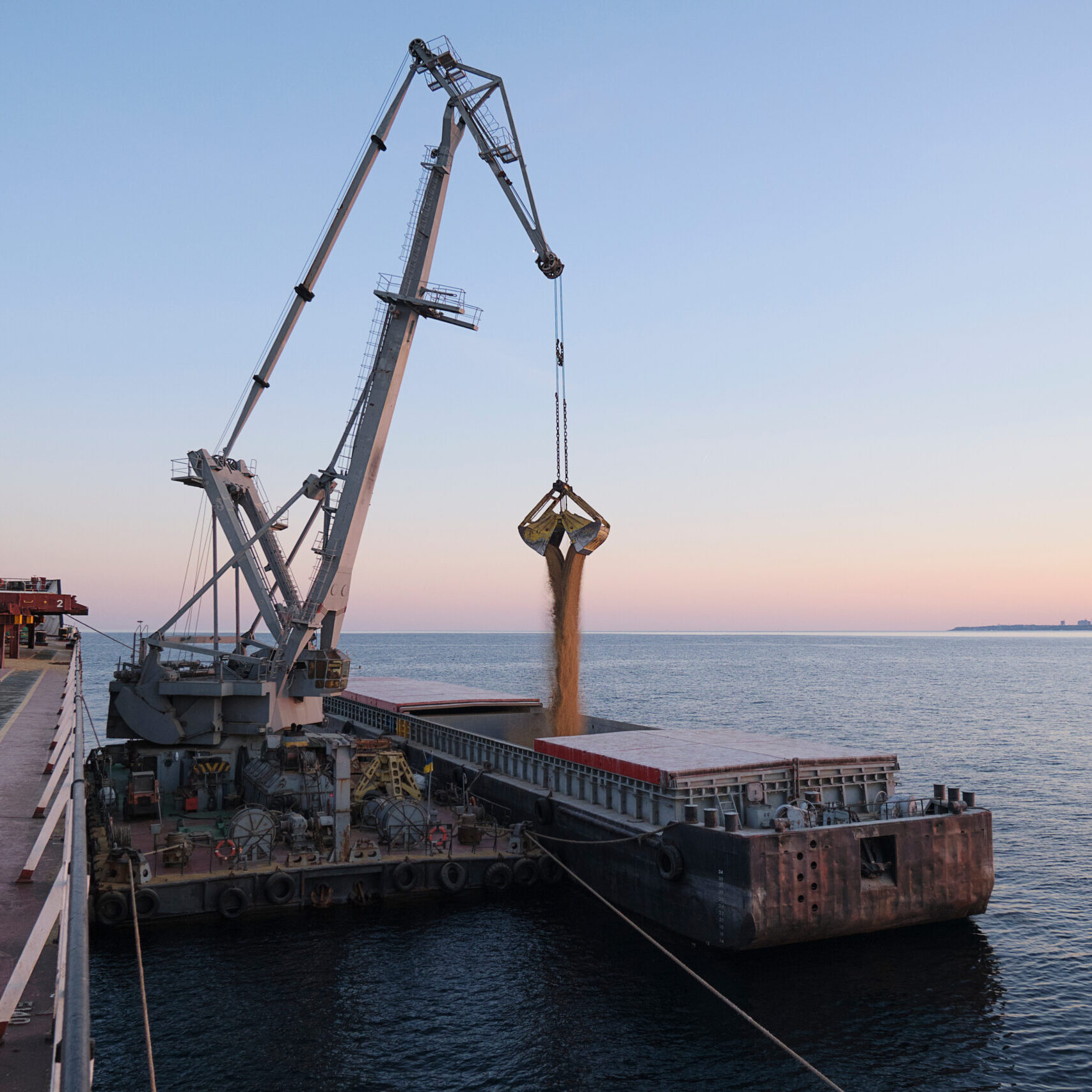 Transshipment of grain products from bulk carrier to the barge on Odessa, Ukraine anchorage during sunset