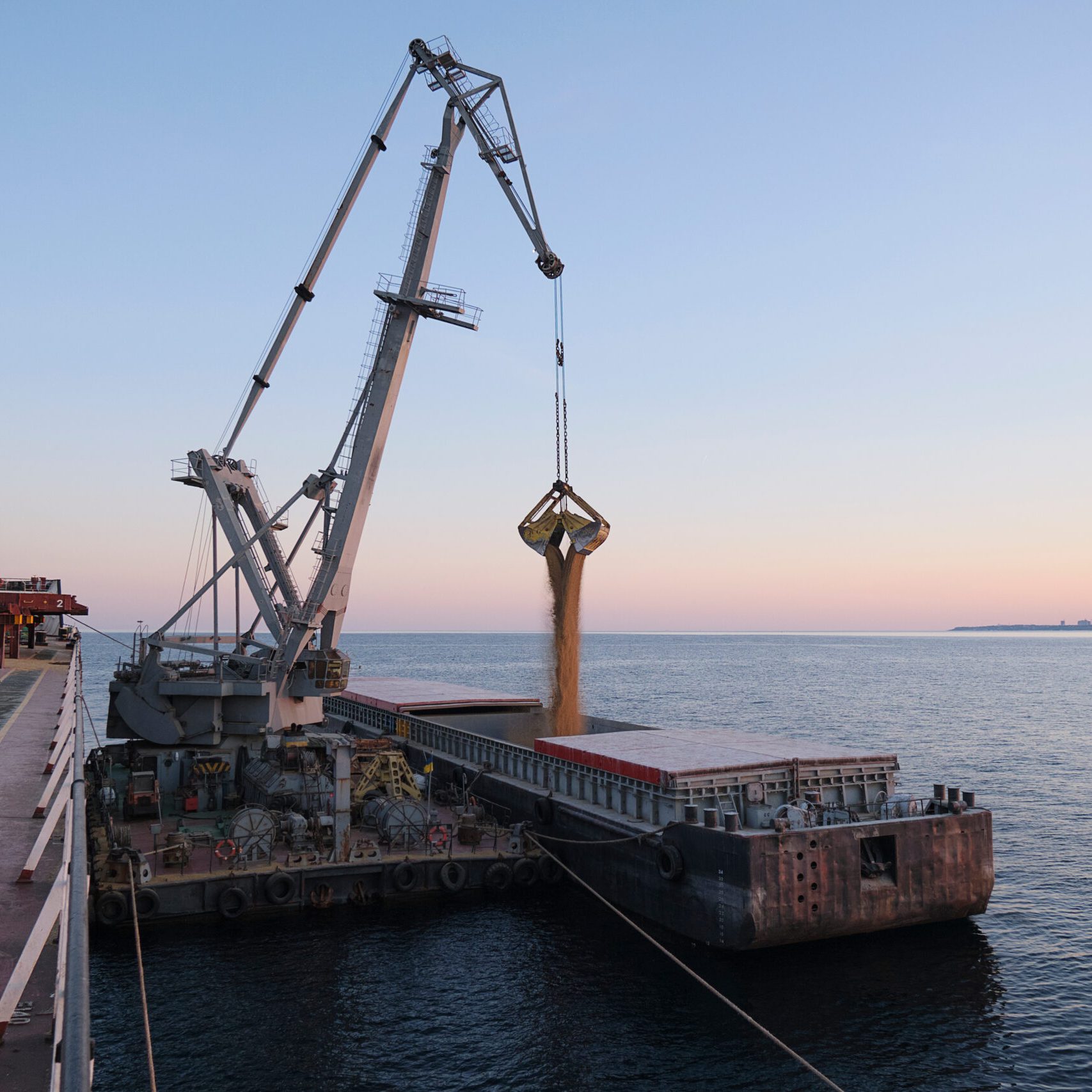 Transshipment of grain products from bulk carrier to the barge on Odessa, Ukraine anchorage during sunset