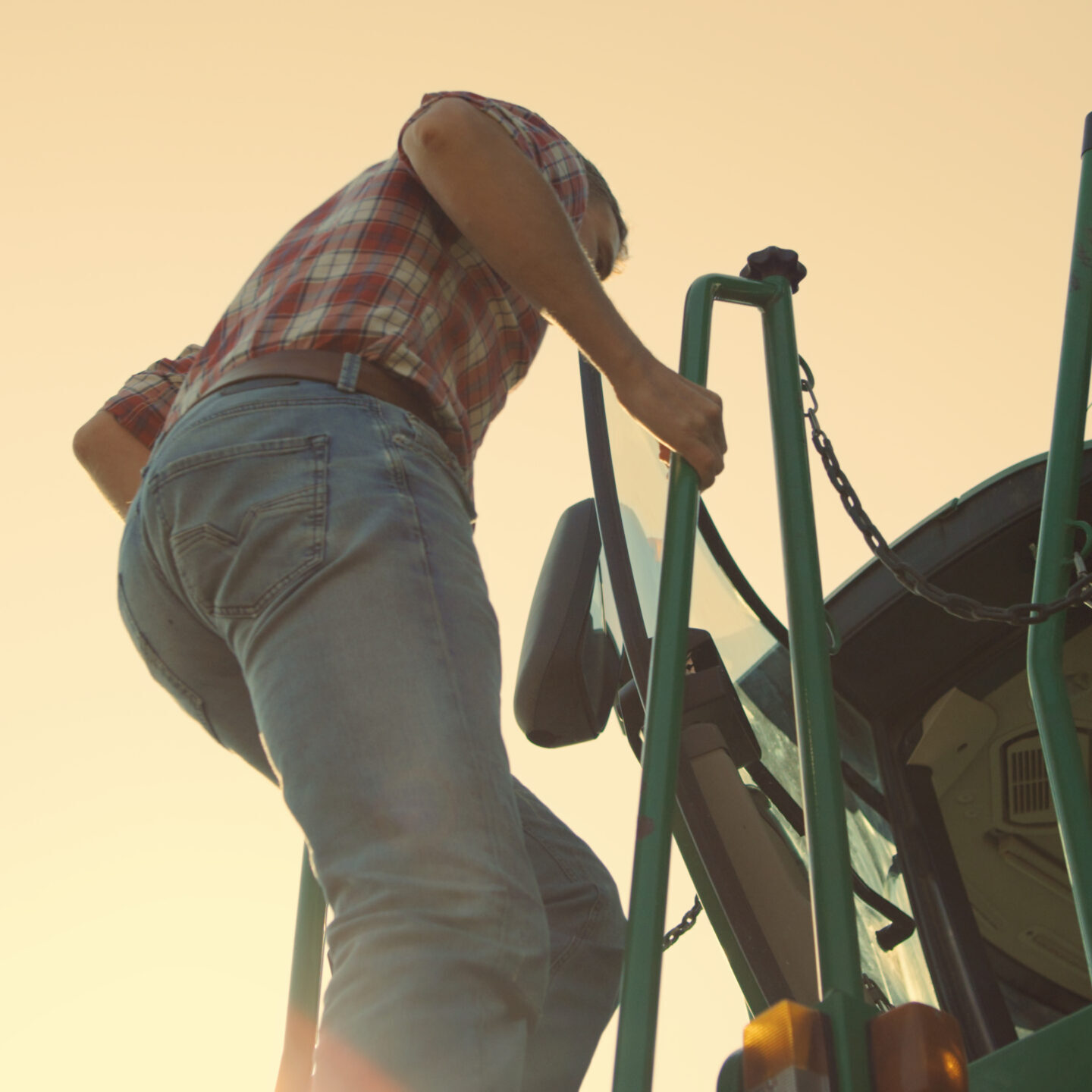 Driver go tractor cabin at sunset. Professional agronomist working on harvesting autumn campaign. Unrecognized farmer operator getting into harvester inspecting machine. Agribusiness worker concept