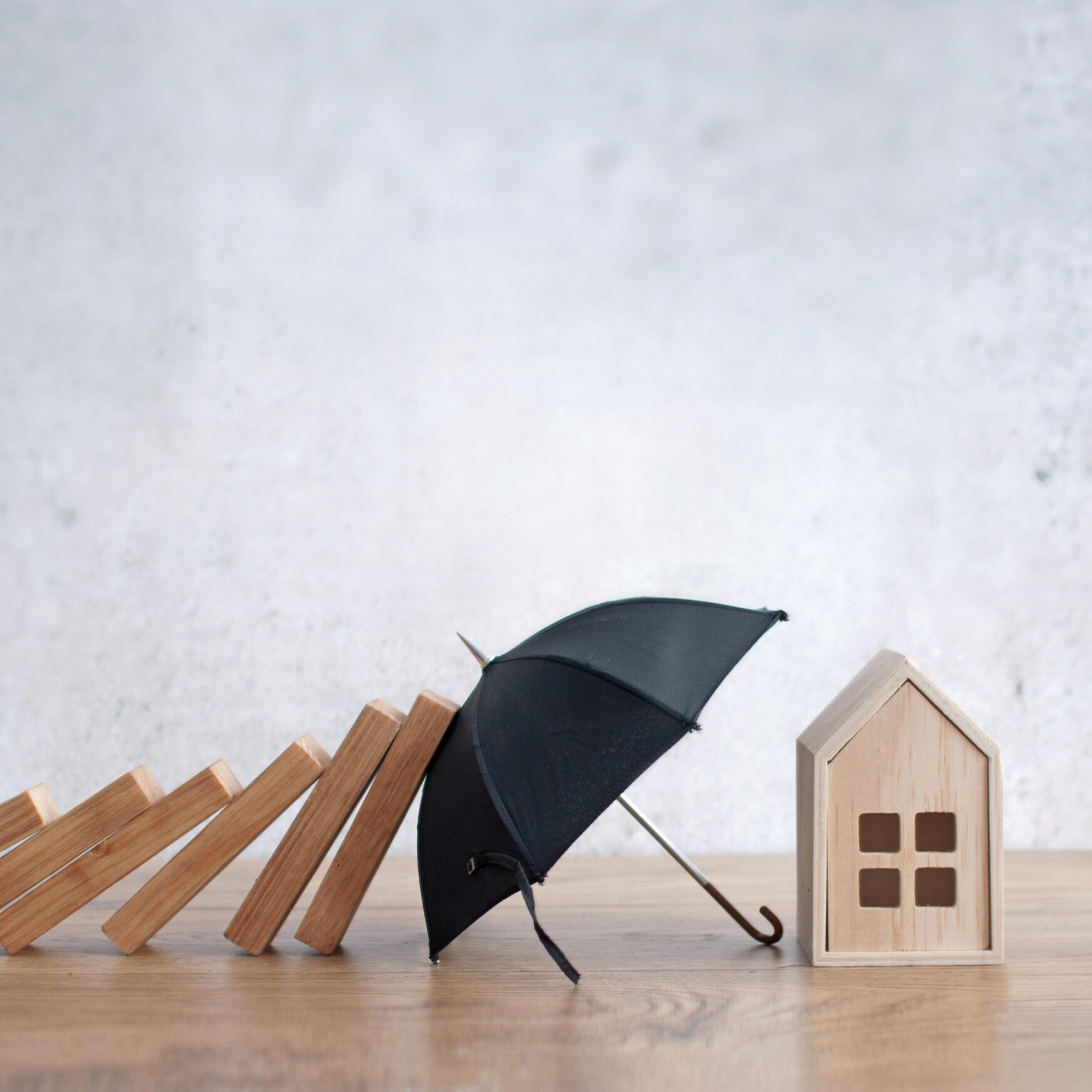 Umbrella protecting house from falling dominoes, insurance concept